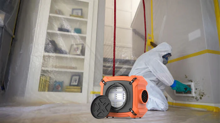 Mold remediation technician in protective gear using an air scrubber in a contained area to remove mold, with plastic sheeting and a bookshelf in the background, emphasizing advanced mold removal techniques.